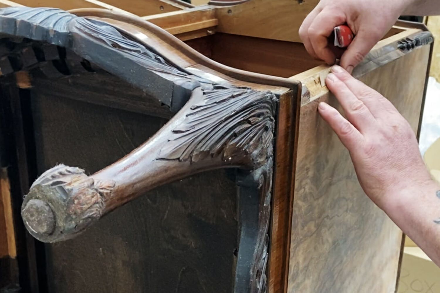 A person meticulously repairs a vintage wooden piece of furniture, focusing on detailed carvings and craftsmanship.