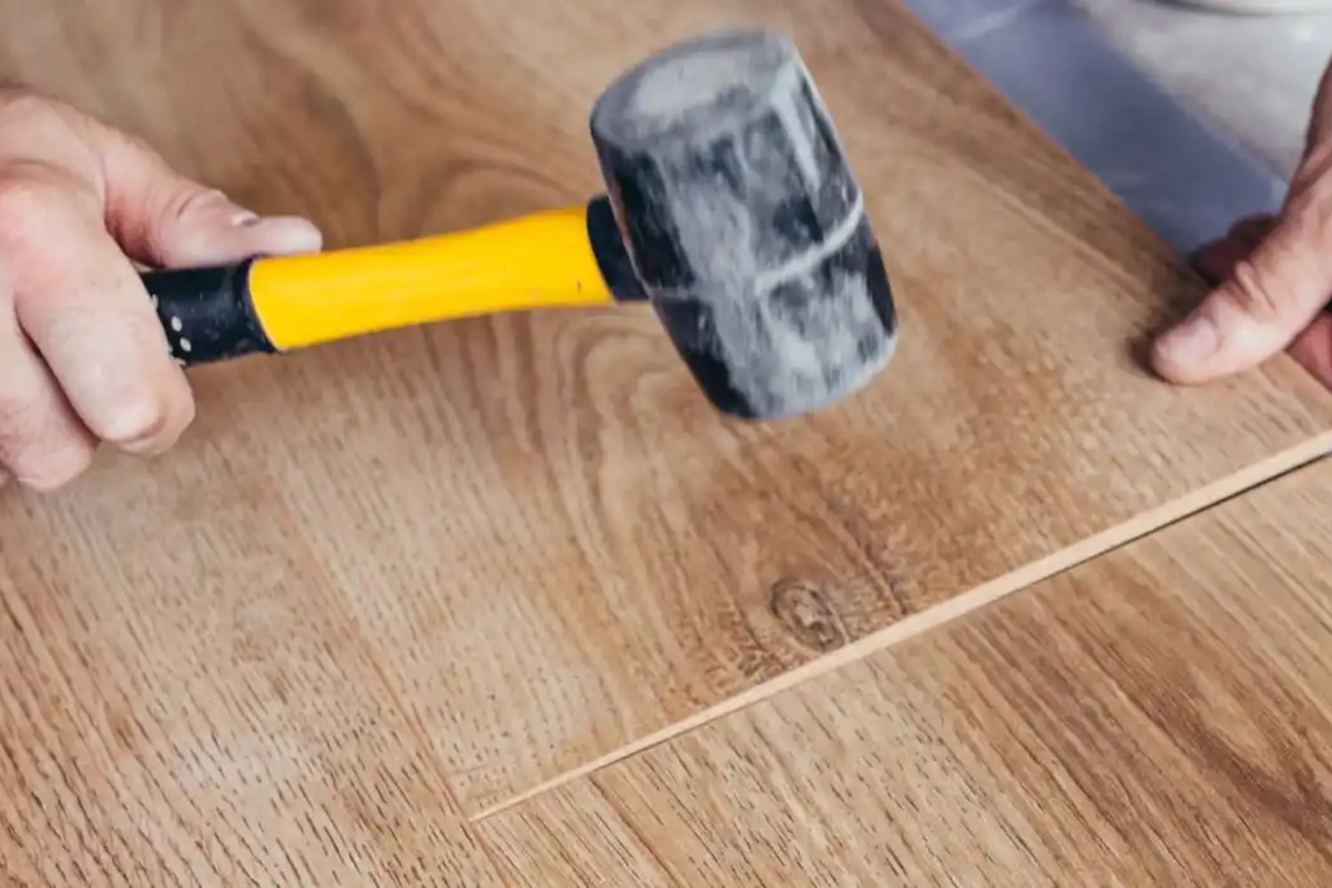 A man using a hammer to install wooden floorboards in a well-lit room, focused on his task.