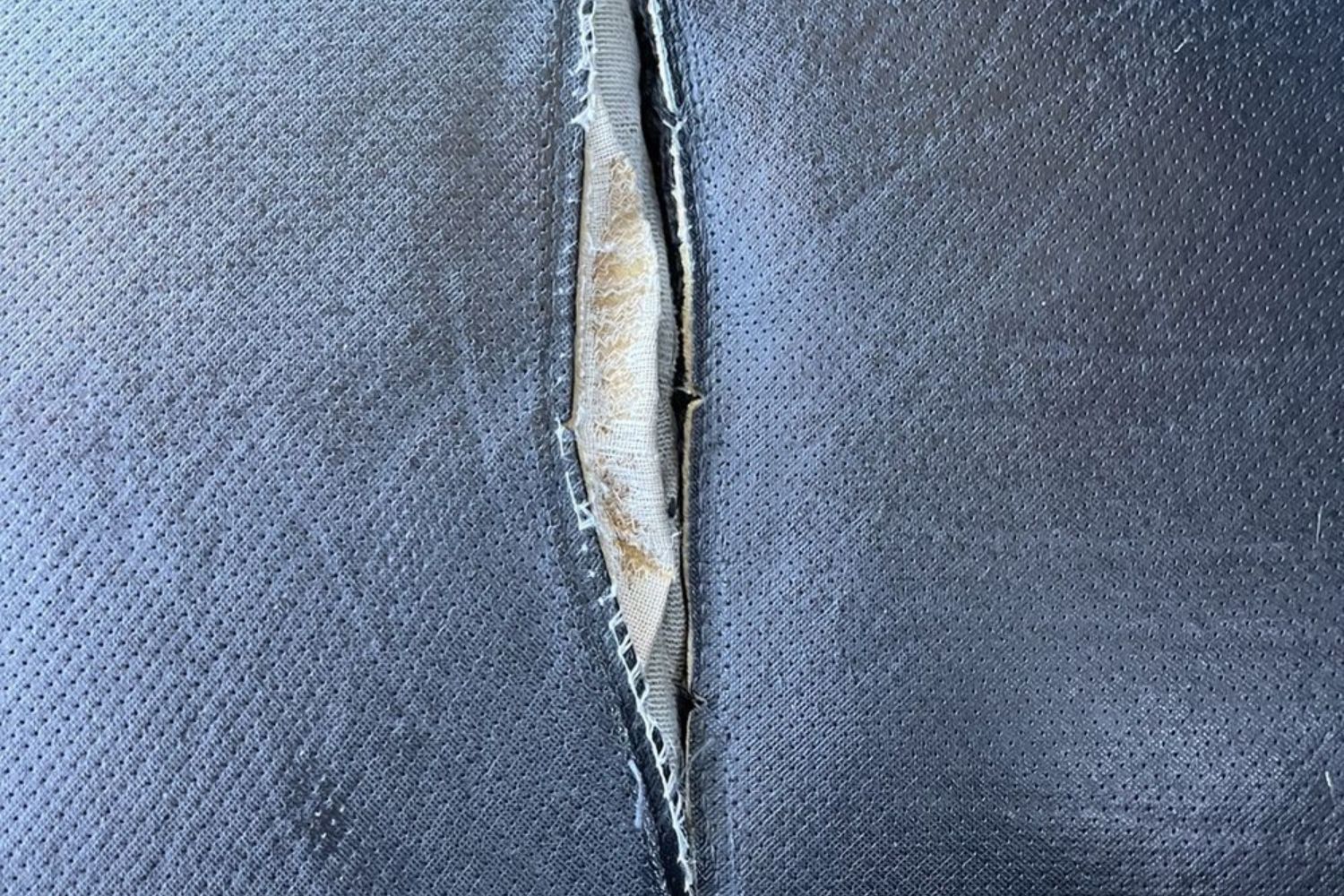 Close-up of a torn blue fabric showing a gap revealing lighter material underneath, highlighting wear and damage.