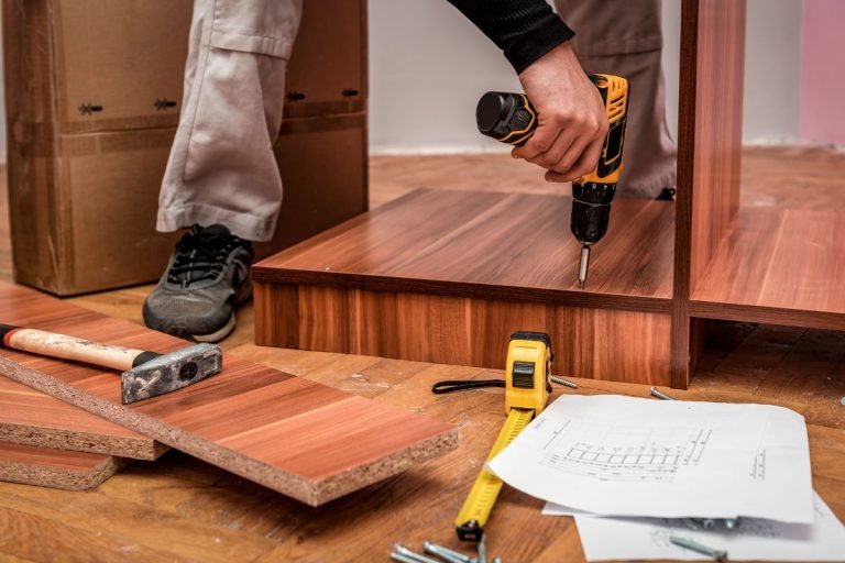 A man operates a drill while constructing a wooden floor for Ashley Furniture Repair